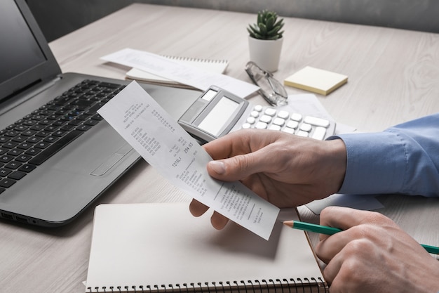 Foto man mano utilizzando la calcolatrice e la scrittura prendere nota con il calcolo dei costi e delle tasse a casa uomo d'affari che fa alcune scartoffie sul posto di lavoro