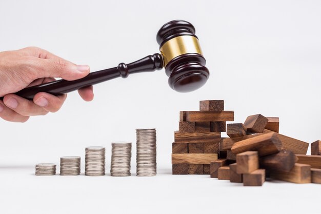 A man hand using wood hammer destroy wood toy building next to row of coins.