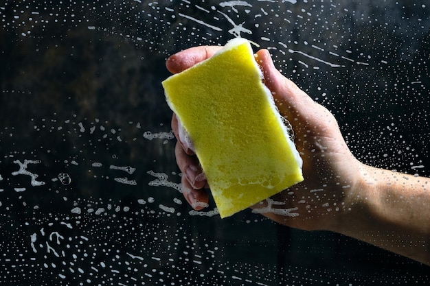 Man hand wast het glas bedekt met schuim, gele spons op een donkere achtergrond.