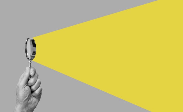 Foto mano dell'uomo con la lente d'ingrandimento raggio giallo proveniente dalla lente di ingrandimento conduzione del concetto di ricerca e analisi di informazioni di controllo spy lavoro di revisore contabile in stile astratto