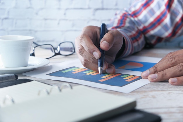 man hand with pen analyzing bar chart on paper