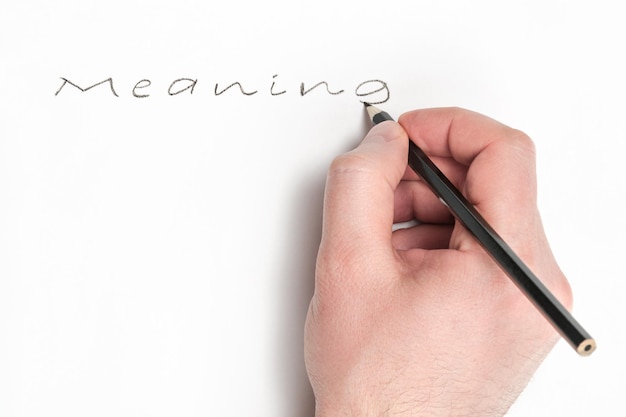 Man hand writes in black pencil a word meaning on white paper