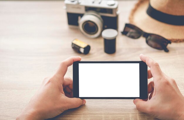 Photo man hand writing a notebook with film camera wicker hat and sunglasses on wooden table - top view