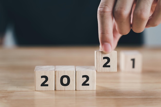 Foto man hand zet houten kubusblok om 2021 jaar te veranderen in 2022 jaar op tafel gelukkig nieuwjaar concept