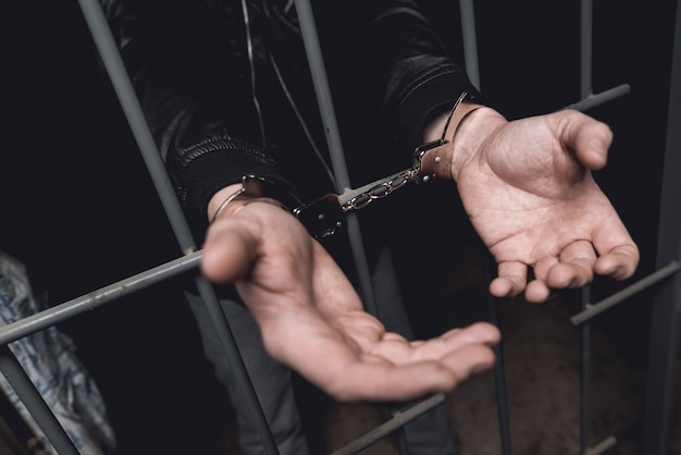 Man In Handcuffs Behind Bars In A Police Station.