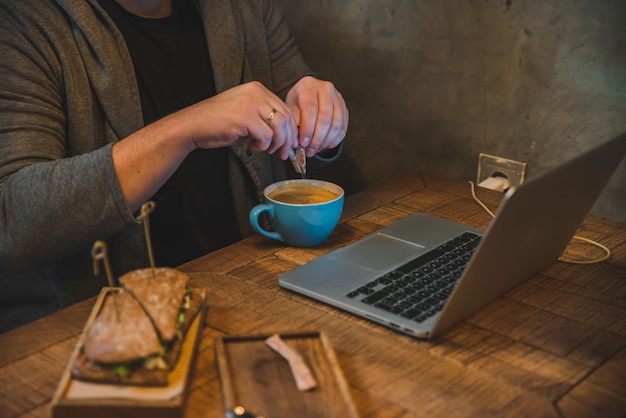 Man handen bezig met laptop in café eten sandwich koffie drinken