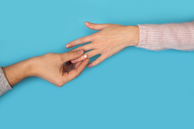 Man handen die trouwring in de vinger van de hand van de vrouw op blauw houden.