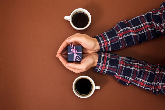 Man handen houden doosgift dichtbij twee koppen van koffie op bruin.