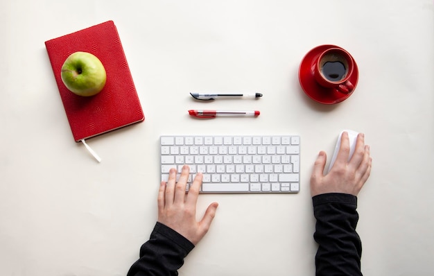 Man handen op draadloos toetsenbord en muis met kopje koffie, pennen, notebooks, groene appel op witte tafel