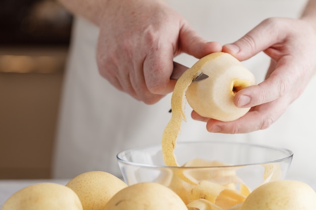 Man handen schillen peer. man schilt fruit aan tafel. zoet ingrediënt voor een heerlijke maaltijd.