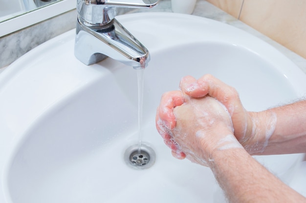 Man handen wassen met zeep onder wastafel in de badkamer.