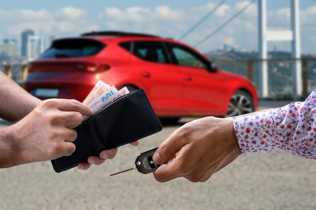 A man handing a car keys next to another man with a red car in