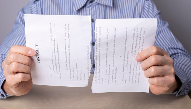 Photo man hands closeup breaking contract termination of agreement deal or employee dismissal concept man sitting at desk in office and holding torn document parts