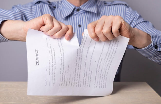 Man hands closeup breaking contract termination of agreement or\
employee dismissal concept man sitting at desk in office and\
tearing document