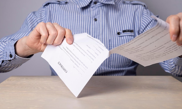 Man hands closeup tearing contract cancellation of deal or
arrangement dismissal concept man sitting at table in office and
breaking document