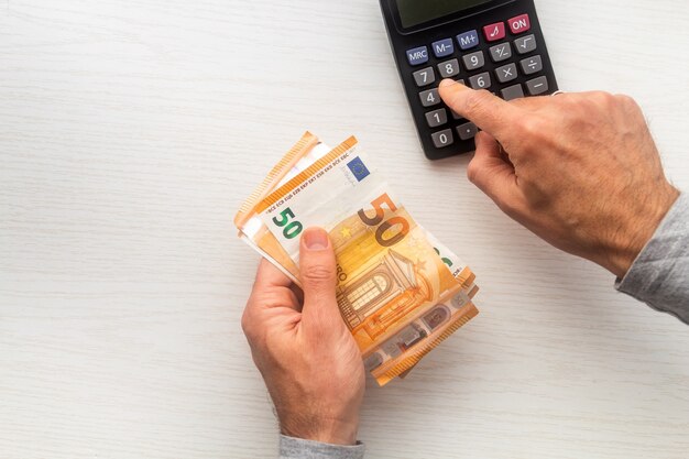 Man hands counting euro cash money banknotes and calculator on white table