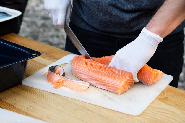 Man hands cutting pink raw salmon with knife on board