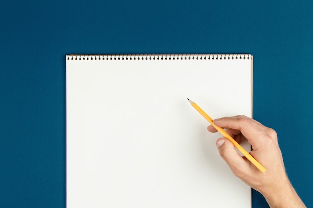 Man hands hold opened notebook pages with pencil, schoolboy doing homework, desk of office worker flat lay. empty notepad on table