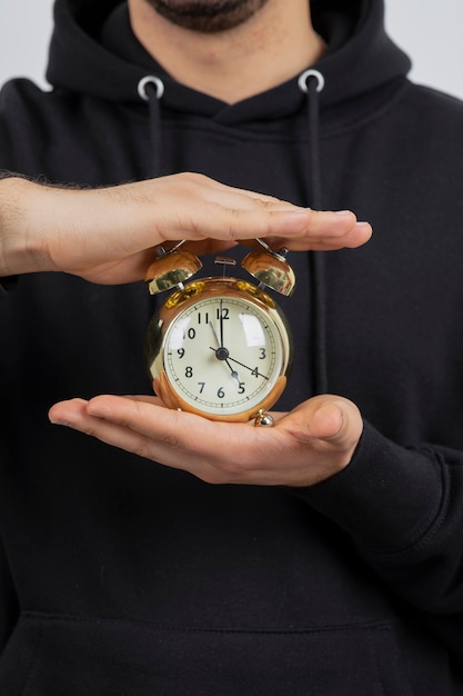 Man hands holding alarm clock against white wall 