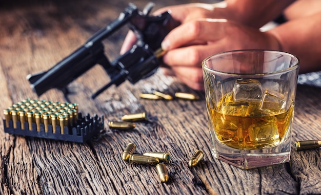 Man hands holding gun and alcohol glass on the table.