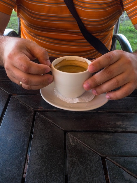 Man hands holding mug of hot espresso that standing on wooden table