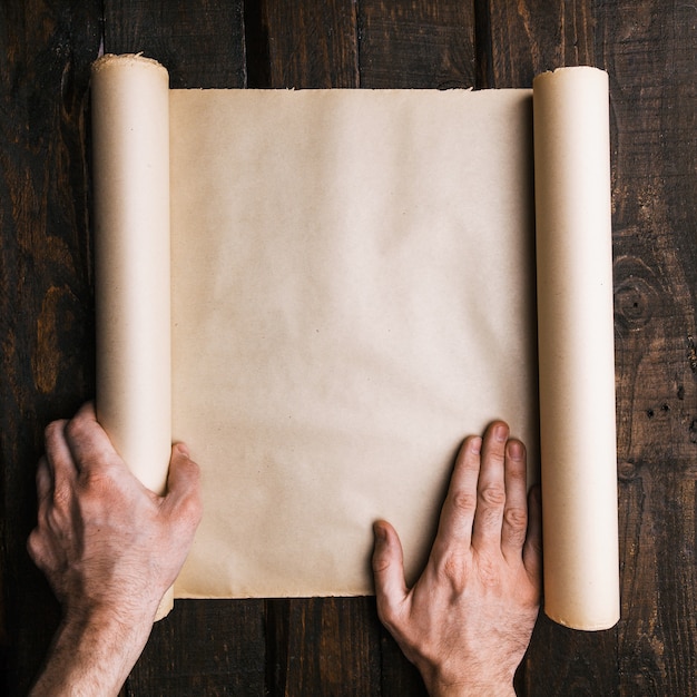 Man hands holding old brown paper scroll on dark wooden planks background. Travel adventure creative minimalistic concept. Treasure seeking, quest flat lay mockup. Room for text, lettering, copy space