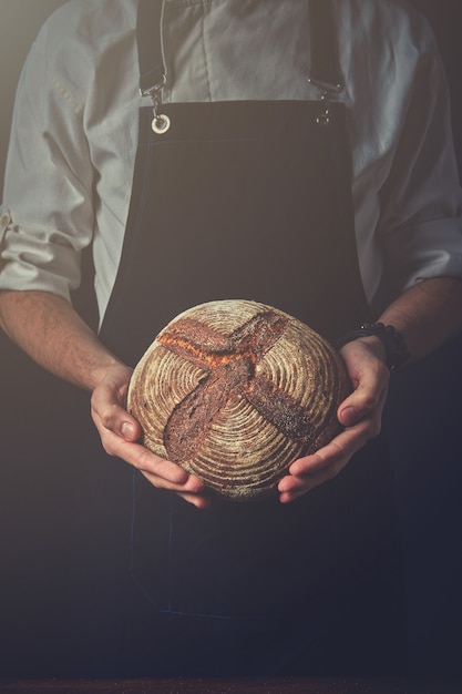 Man hands holding round dark bread, blurred background