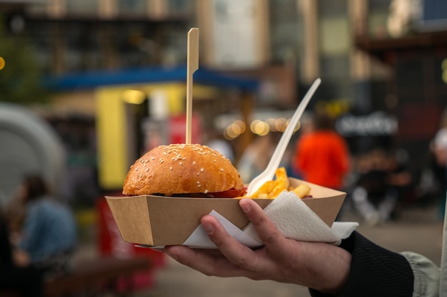 Man hands holding street food burger with french fries on craft paper