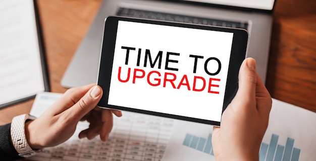 Photo man hands holding tablet with text time to upgrade at workplace. businessman working at desk with documents