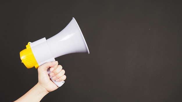 Man hands is holding yellow megaphone on black background.