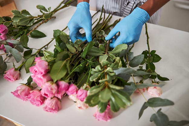 man hands in latex gloves while he is creating fresh bouquets of pink roses