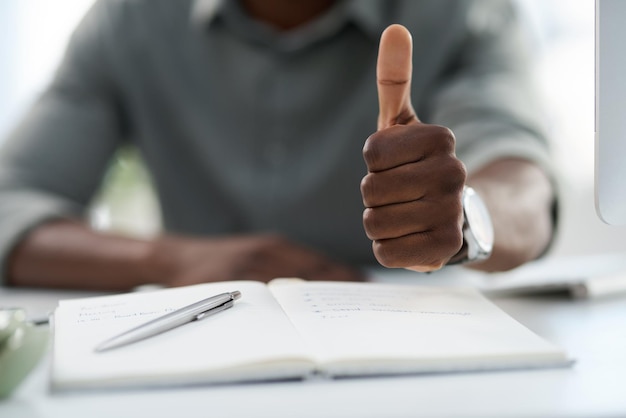 Photo man hands and notebook with thumbs up for winning achievement or good job on office desk hand of male person with book in planning showing thumb emoji yes sign or like for approval at workplace