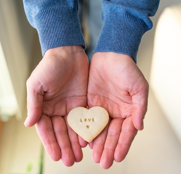 Foto mani dell'uomo che offrono biscotto a forma di cuore. lettere amore. il giorno di san valentino concetto.