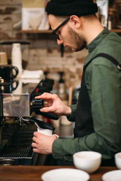Руки человека наливают напиток из кофеварки.