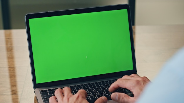 Foto uomo che scrive con le mani sul portatile chromakey sul posto di lavoro, primo piano, capo che preme i pulsanti