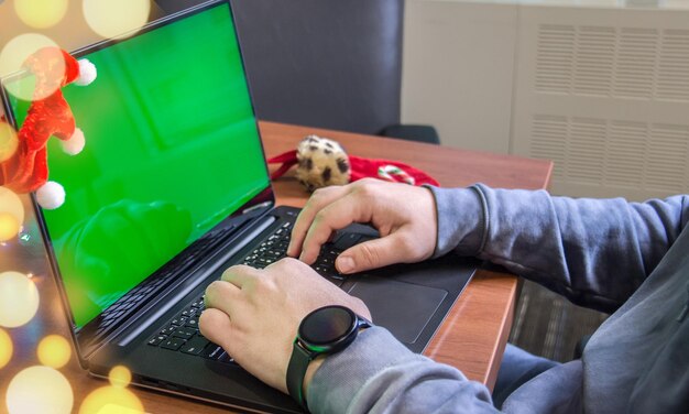 Foto mani dell'uomo che scrive sulla tastiera del portatile con schermo verde vuoto e decorazione natalizia sullo sfondo