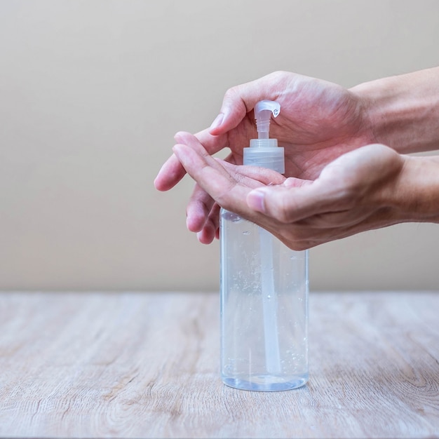 Equipaggi le mani facendo uso della bottiglia del gel o del disinfettante dell'alcool della mano del lavaggio