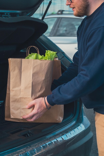 man hands with groceries bags put it in car trunk close up