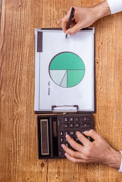 Man hands writing in the document and using a calculator.