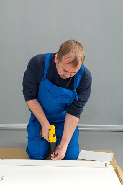 A man, a handyman in a blue jumpsuit, is assembling a table in close-up