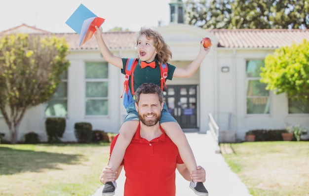 Man and happy amazed child piggyback near school father walking son to school parent and pupil of pr