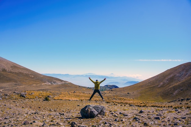 Foto uomo felice di saltare a braccia aperte in cima alla montagna