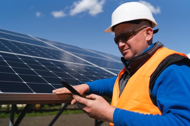 Man in hard hat using smartphone on the background of solar panels