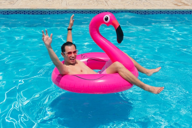 A man has fun on a fuchsia flamingo inflatable float in the pool.