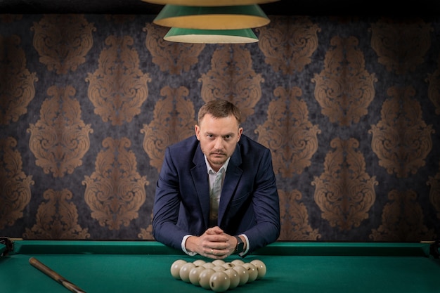 A man has placed balls on the pool table and is ready to play a game