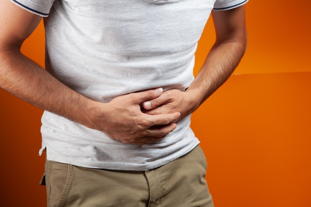 man has a stomach ache on orange background