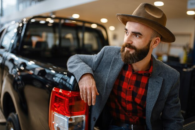 Man in hat poses at new pickup truck in car dealership.