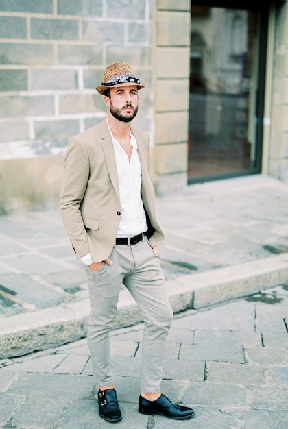 Photo man in a hat stands on the paving stones near the stone building