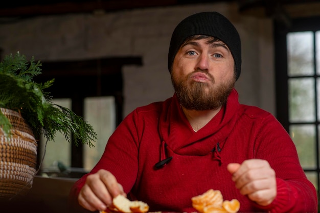 A man in a hat and sweater eats a tangerine