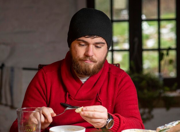 A man in a hat and sweater has breakfast in the kitchen